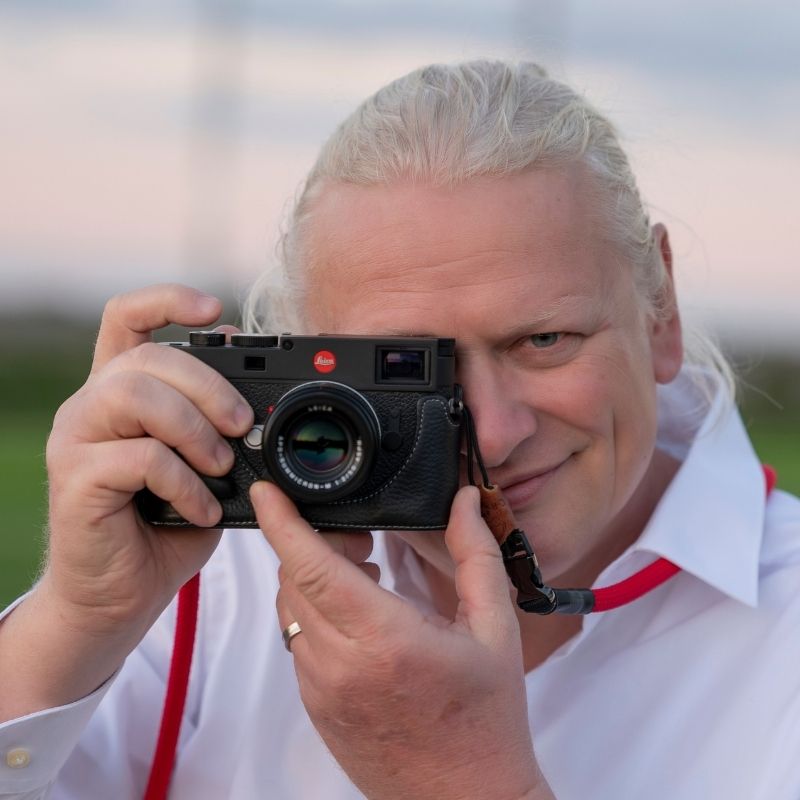 Franz Paul Podek – Pferdefotograf mit Blick für den Moment Franz Paul Podek hält eine Leica-Kamera vors Auge und blickt lächelnd in die Linse